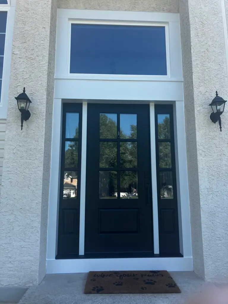 Elegant black front door with large glass panels, flanked by wall sconces, and a welcome mat, symbolizing quality door installation services by Azinex Construction.