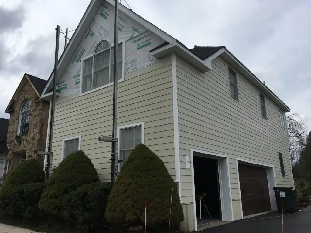 Siding installation on a residential home, showcasing freshly applied HardieWrap, scaffolding, and well-maintained landscaping, emphasizing exterior home improvement by Azinex Construction.